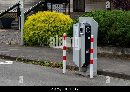 Ladestation für Elektrofahrzeuge auf der Fahrbahn, markiert durch rote und weiße Pole zur Sicherheit. In der Nähe gibt es einen lebhaften grünen Sträucher, der den Hauch von Natur verleiht Stockfoto