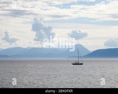 Segelyacht vor der Isle of Skye, Schottland, mit dramatischen Highland-Bergen und weichen Wolken im Hintergrund Stockfoto