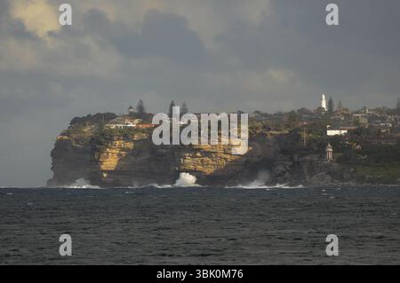 Dramatische Klippen und Häuser an der Küste unter einem stimmungsvollen Himmel in Sydney, Australien. Stockfoto