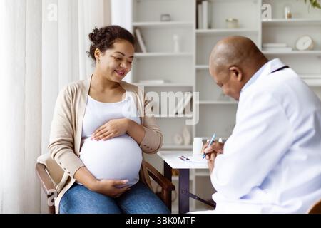 Schwangerschaftskontrolle. Professioneller schwarzer Geburtshelfer, der den Patienten anhört und Aufzeichnungen schreibt Stockfoto
