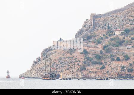 ALANYA, TÜRKEI, 10.12.2018: Drei Piratenschiffe im Vintage-Stil fahren in der Nähe einer felsigen Klippe mit einer alten Festung. Die ruhige Meereslandschaft und die Histori Stockfoto