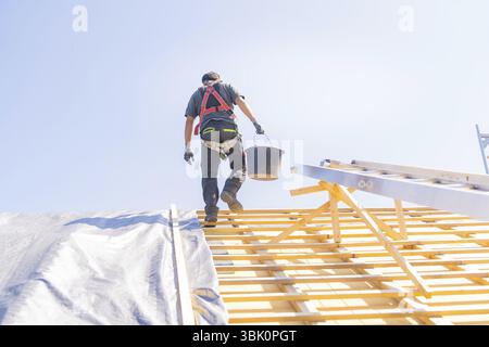 Ein Arbeiter in Sicherheitskleidung klettert auf eine Leiter, um bei sonnigem Wetter auf einem Dach zu arbeiten, Dachsanierung, Hausbau, Pforzheim, Deutschland, Europa Stockfoto