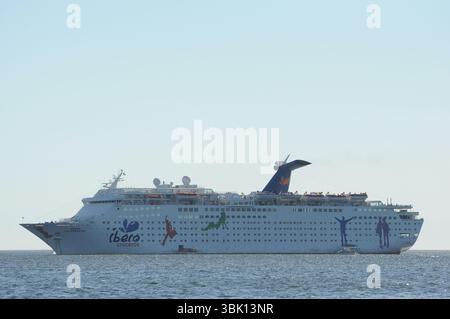Das Kreuzfahrtschiff Ibero Cruceros wird auf ruhigen Gewässern unter einem klaren blauen Himmel gefangen. Das Schiff verfügt über lebendige, farbenfrohe Grafiken auf der Seite, SH Stockfoto