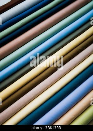 Nahaufnahme zahlreicher Stoffrollen, die in diagonalen Reihen angeordnet sind und eine Vielzahl von Farben und Texturen zeigen. Stockfoto