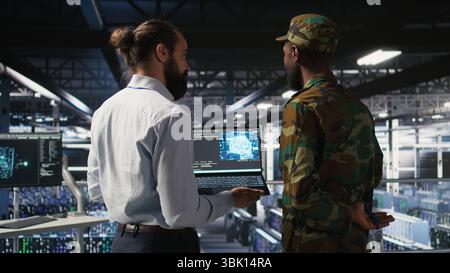 Militärtechniker in sicheren Rechenzentren nutzen Laptops zur Überwachung von Systemen der künstlichen Intelligenz. Militärangehörige im Server-Hub sorgen für eine stabile Infrastruktur für maschinelles Lernen Stockfoto
