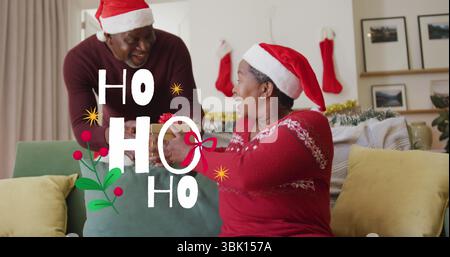 Ein Mann mit Weihnachtsmann, der der Frau auf dem Sofa im Wohnzimmer ein Geschenk mit Band gibt, mit Strümpfen und Tönung Stockfoto