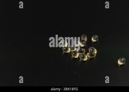 Transparente Kapseln sind auf einer dunklen Oberfläche verstreut und zeigen in dieser Nahaufnahme ihre glänzende Textur und ihre besondere Form. Stockfoto