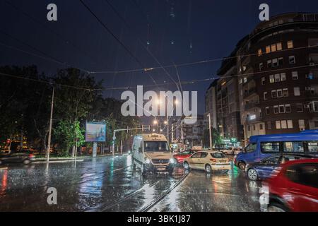 BELGRAD, SERBIEN - 22. APRIL 2025: Nächtlicher Regen tränkt die belebte Trosarina-Kreuzung in Belgrad, während die Autos stehen und ihre Scheinwerfer auf slic reflektieren Stockfoto