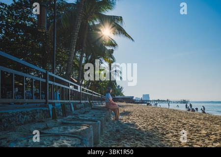 Die Frau sitzt im Schatten von Palmen, in der Ferne können andere Strandgänger die ruhige Küstenlandschaft in Balikpapan, Indon, genießen Stockfoto