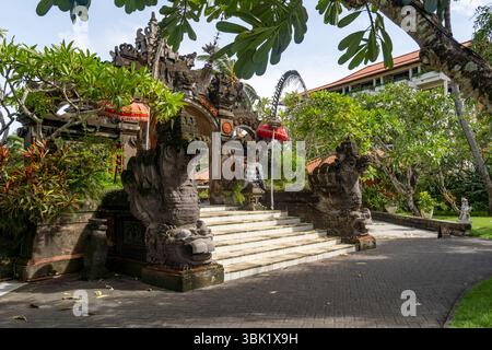 Bali, Indonesien - 19. Dezember 2024: Schöner Garten mit einem Steinbogen und Stufen, die hinauf führen. Der Bogengang ist mit roten und weißen Blumen dekoriert Stockfoto