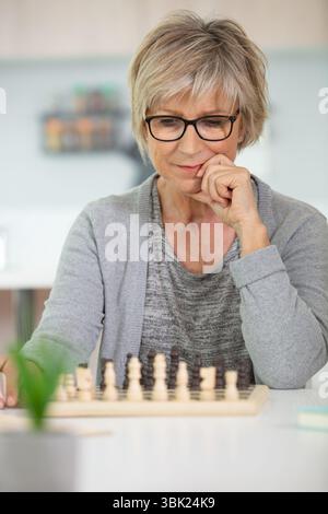 Seniorin spielt Schach, glücklich, allein auf dem Sofa zu sitzen Stockfoto