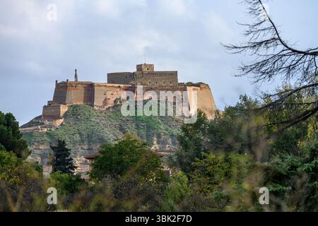 Eine beeindruckende historische Burg auf einem Hügel, mit Steinmauern, befestigten Strukturen und einem malerischen grünen Hügel mit einem hellblauen Himmel. Stockfoto
