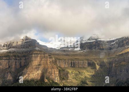 Hoch aufragende Klippen mit Blick auf einen dichten Wald und schneebedeckte Gipfel schaffen einen atemberaubenden Kontrast aus Texturen und Farben. Stockfoto