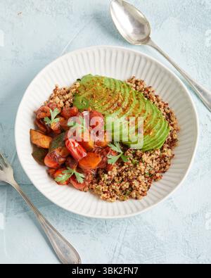 Gesunde Quinoa-Schüssel mit Avocado, Nüssen und Tomaten – ein farbenfrohes, pflanzliches Mittag- oder Abendessen. Stockfoto