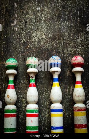 Vier Vintage-Bowlingnadeln aus Holz mit lebhaften Farben sitzen in einer Reihe auf einer rustikalen Holzoberfläche Stockfoto