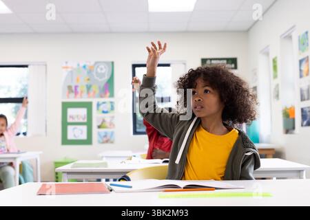 Im Klassenzimmer, ein neugieriger Junge, der die Hand erhebt, begierig darauf, die Frage des Lehrers zu beantworten, in der Schule Stockfoto