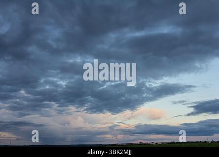 Weitläufiger Himmel mit dramatischen Wolkenformationen bei Sonnenuntergang über einer ruhigen Landschaft mit sanften Farben. Stockfoto