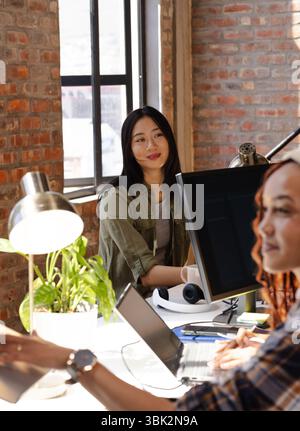 Asiatische Frau, die mit einem Kollegen am Schreibtisch zusammenarbeitet und am Computer codiert Stockfoto