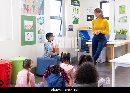 Lehrerin, die verschiedene Schüler in Klassenzimmer-Recycling-Unterricht einbezieht, Kinder zuhört, in der Schule Stockfoto