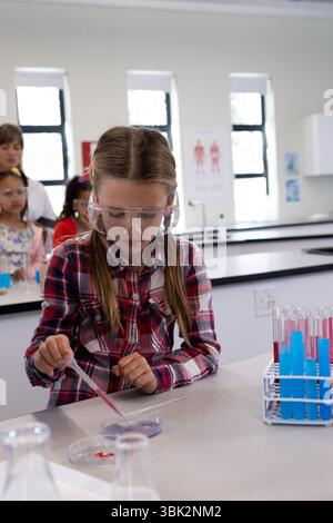 In der Schule führte ein Mädchen mit Schutzbrille ein wissenschaftliches Experiment mit Pipette durch Stockfoto