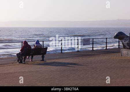 Zwei Walker sitzen auf dem Filey-Abschlussball und schauen sich ihre Handys an Stockfoto