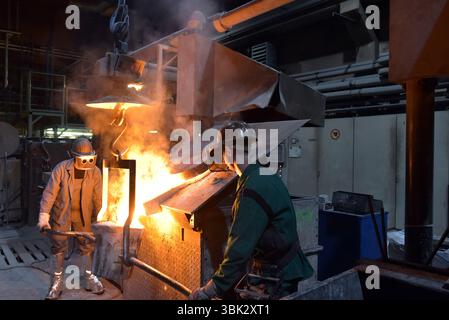 Arbeitnehmer in einer Gießerei gießen ein Werkstück aus Metall - Sicherheit bei der Arbeit und Teamarbeit Stockfoto