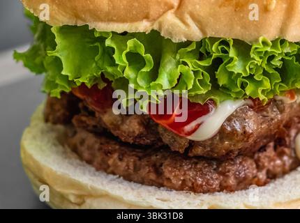 Hausgemachter Doppelburger mit Käse, Gemüse und Saucen. Leckerer Burger mit eingelegtem Rindfleisch, Zwiebeln, Salat und Sauce. Junk Fast Food. Hamburge Stockfoto