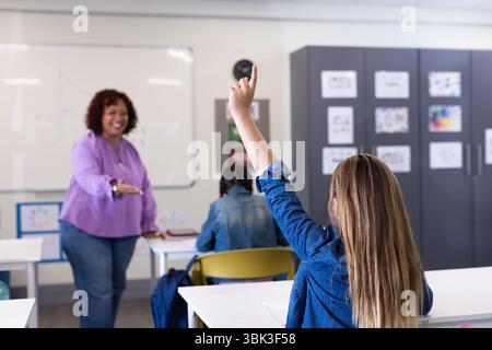 Die Schülerin hebt die Hand im Klassenzimmer, während die Lehrerin lächelt und sich in der Schule engagiert Stockfoto