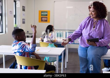 Weibliche Lehrerin, die sich mit Schülern beschäftigt, die Hand im Unterricht heben, aktives Lernen fördern, in der Schule Stockfoto