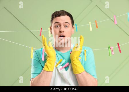Verwirrter junger Mann mit hängenden Wäscheleinen und Plastiktüchern auf grünem Hintergrund Stockfoto