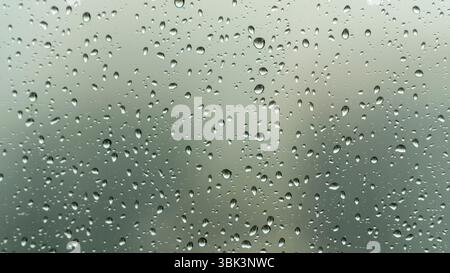Nahaufnahme von Regentropfen an einem Glasfenster an einem regnerischen Tag, mit einem weichen, verschwommenen Hintergrund, der eine ruhige und stimmungsvolle Atmosphäre schafft. Stockfoto