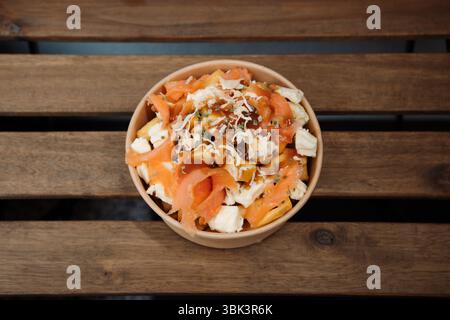 Poutine-Pommes mit Käse und Lachs in Papierbehälter zum Mitnehmen. Köstliche, frisch zubereitete Mahlzeit, perfekt für Menüs, Restaurants oder Lieferservice Stockfoto