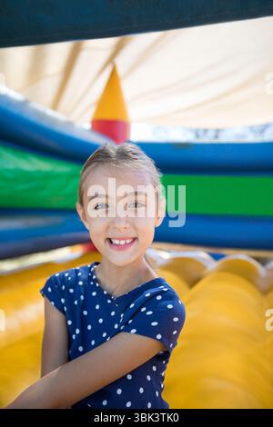 Mädchen, das vor der aufblasbaren Rutsche in der Spielzone im Freien steht und ein marineblaues Polka Dot-Shirt trägt Stockfoto
