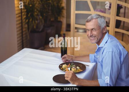 Senior Mann hält Gabel und Messer am Restauranttisch mit Teller und Wein, Kopierraum Stockfoto