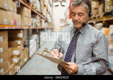 Leitender männlicher Vorgesetzter im Anzug mit Checkboxen in Lagerregalen, Kopierraum Stockfoto