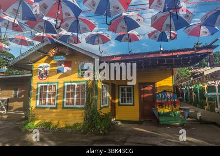 Das gelb gemalte Gemeinschaftsbrett, dekoriert mit Regenschirmen mit Panamesischen Nationalflaggendrucken in Old Bank, Isla Bastimentos, Bocas del Toro, Panama Stockfoto