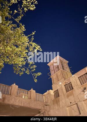Nächtlicher Blick auf ein Dach im traditionellen arabischen Stil in Al Seef, Dubai, mit Bäumen im Vordergrund und sanfter Beleuchtung. Stockfoto
