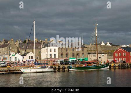 Lerwick Harbour sonnt sich in der frühen Sonne, während sich über dem Himmel dunkler, brütender Himmel erhebt – ein dramatischer Kontrast zu Shetlands wechselndem Wetter. Stockfoto