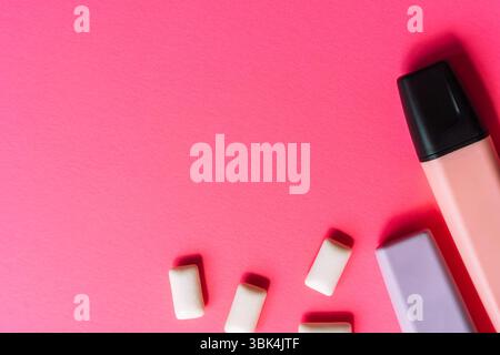 Kaugummi, ein rosafarbener Textmarker und ein lila Radiergummi auf leuchtendem rosa Hintergrund. Flaches Design mit auffälliger Gen Z-Ästhetik. Stockfoto