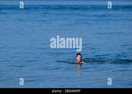 Eine Schwimmerin genießt das Wasser am Strand von Exmouth in Devon, da für den größten Teil Englands gelbe Hitzewarnungen ausgegeben wurden. Stockfoto