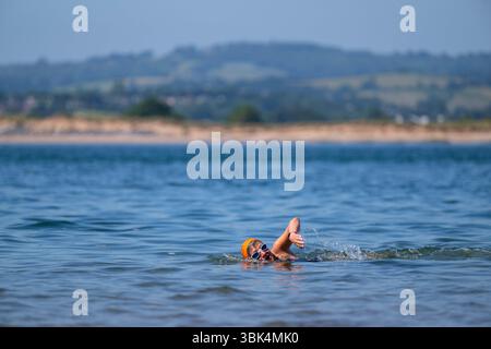 Eine Schwimmerin genießt das Wasser am Strand von Exmouth in Devon, da für den größten Teil Englands gelbe Hitzewarnungen ausgegeben wurden. Stockfoto