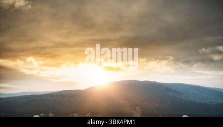 Das flache Design zeigt Sonnenstrahlen, die durch bewölkte Wolken über dem immergrünen Bergrücken strömen Stockfoto