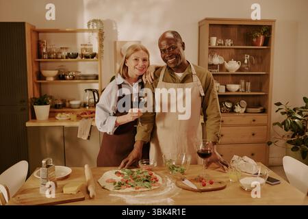 Senior Kaukasierin und Senior Black man lächeln, während sie zusammen Pizza machen Stockfoto