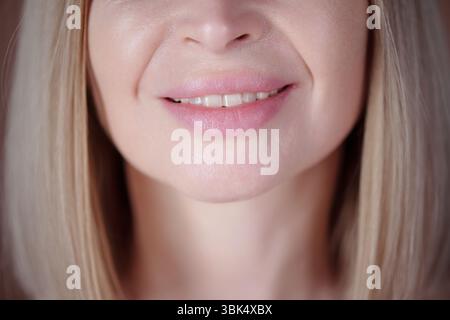 Close-up shot featuring smiling womans lips and chin, highlighting her pink lips and smooth skin. Details show blonde hair framing her face Stockfoto