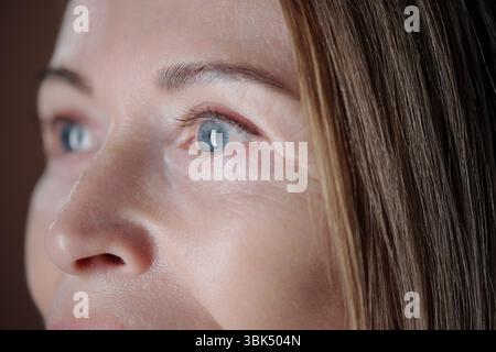 Nahaufnahme des Gesichts der Frau in sanfter Beleuchtung mit detaillierter Hautstruktur und reflektierenden blauen Augen sowie glatten, natürlichen Gesichtszügen, die ihren ruhigen und ruhigen Ausdruck betonen Stockfoto
