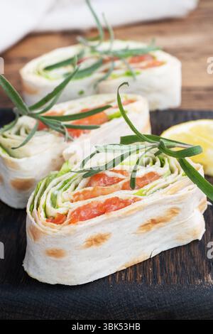 Dünnes Fladenbrot und rot gesalzener Lachs mit Salatblättern auf einem hölzernen Schneidebrett Stockfoto