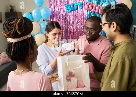 Gruppe junger Erwachsener multiethnischer Freunde, die Gender Reveal Party feiern, lächeln und Babyschuhe und Geschenktüte halten Stockfoto