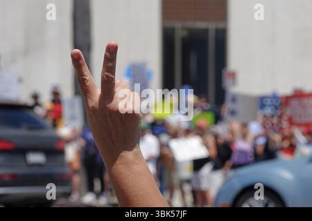 Eine Hand, die zwei Finger als Friedenszeichen hochhält, wird während einer politischen Kundgebung in einer Stadt aus nächster Nähe gezeigt. Stockfoto