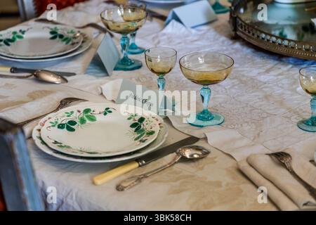 Der gedeckte Tisch im Speisesaal des George-Sand-Hauses (Maison de George Sand) am Place Sainte-Anne in Nohant, Gemeinde Nohant-Vic, im Berry, Département Indre, Centre-Val de Loire, Frankreich, zeigt das Gedeck von Frédéric Chopin. Eine Platzkarte trägt seinen Namen. Chopin war neun Jahre lang (1837–1847) in einer Beziehung mit George Sand. Die Porzellanteller der Fabrik Creil-Montereau haben ein grünes Blattmuster mit roten Beeren. Neben ihnen stehen Coupe-Gläser mit türkisfarbenen Stielen (möglicherweise die farbigen Kristallgläser, die Chopin geschenkt hat), und silbernes Besteck liegt auf einer Stickerei Stockfoto
