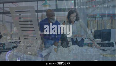 Lehnende Architekten prüfen Baupläne auf dem Tisch in modernen Büros, mit Laptops und Dokumenten Stockfoto